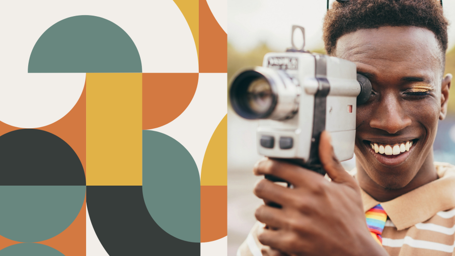 A young Black filmmaker is holding a Super 8 camera up to his eye, whilst smiling.