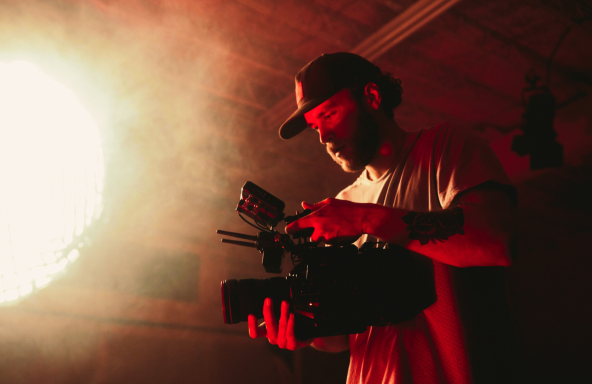 A camera operator is in a studio with a handheld camera. In front of him is a bright ball of light.