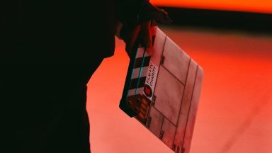 A close up of a person holding a clapperboard behind their back. On the board is the Film and TV Charity logo