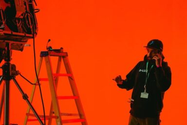A crew member is on the phone in a brightly lit film studio. There is lighting equipment around him.
