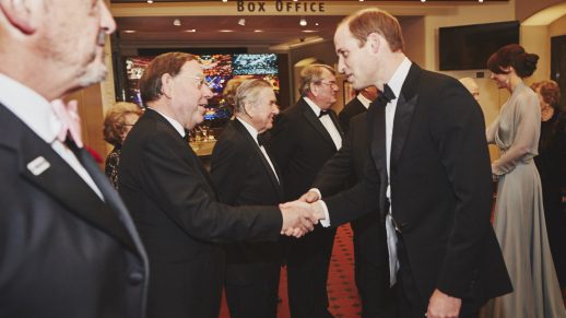 Prince William wearing a black tuxedo, greeting a group of guests inside the Leicester Square ODEON cinema, ahead of the premiere of Spectre, at the Royal Film Performance in 2015.