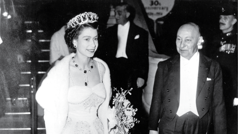 Queen Elizabeth II is escorted by Reginald Bromhead, the Chairman of the Cinematograph and Trade Benevolent Fund, as she leaves the Royal Film Performance in Leicester Square. Taken in 1954.