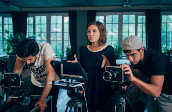 Three crew members are on set in a house setting. Two of the workers are standing behind Blackmagic cameras, whilst the other is standing in the middle directing whoever is in front of the camera.