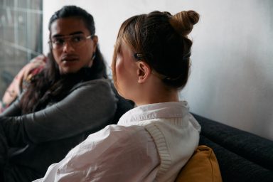 A woman is sat with her back to the camera. She is talking to another person who is sat facing her, paying attention to what she is saying.