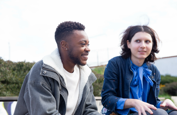 Two young colleagues are sat in an outdoor open space.