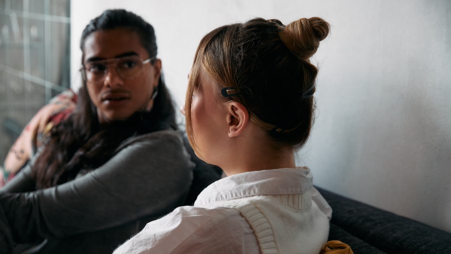 A woman is sat with her back to the camera. She is talking to another person who is sat facing her, paying attention to what she is saying.