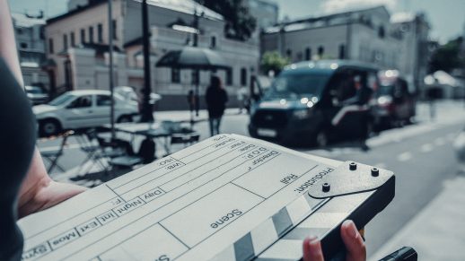 Close-up shot of a crew member with a clapperboard on set. In the background is a street set.