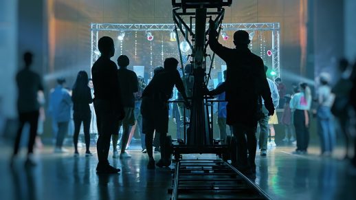 A TV crew being silhouetted by lights as they set up a camera on tracks