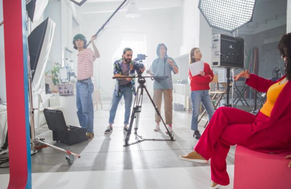 A film crew are set up and filming a presenter that is doing a to-camera piece.
