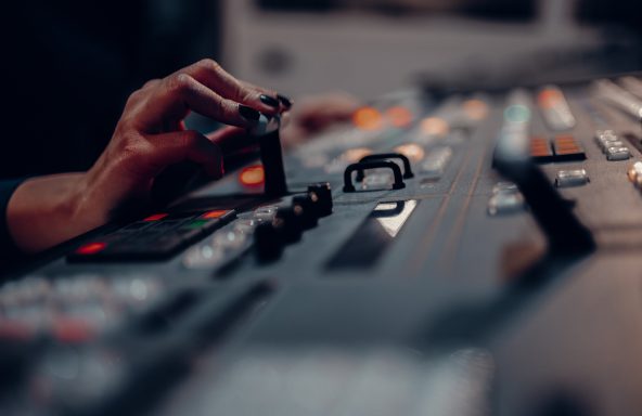 A vision mixer's hand with painted nails using a vision mixing desk for television production.