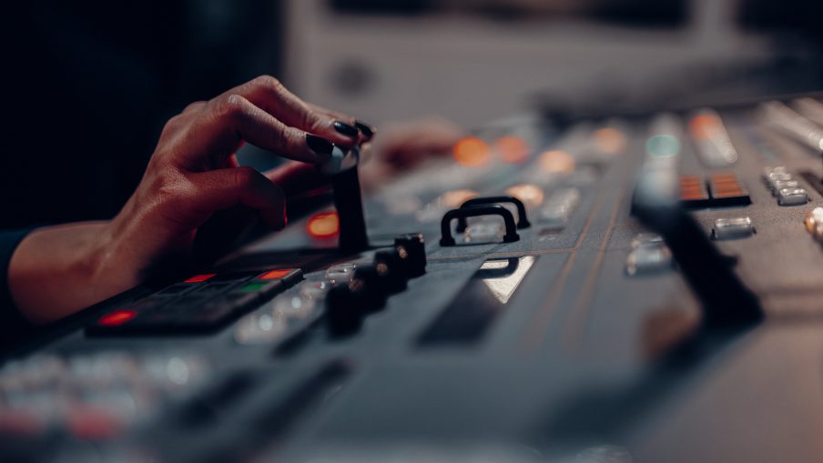 A vision mixer's hand with painted nails using a vision mixing desk for television production.